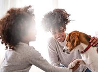 young girl with curly hair smiling and petting beagle with her mom smiling at her
